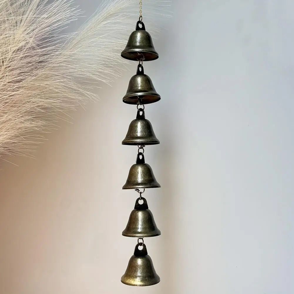 A vertical arrangement of small, antique bronze iron wind chimes hanging from a feathery plume.