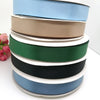 A stack of double face satin ribbon in various solid colors including blue, beige, cream, green, black, and gray.