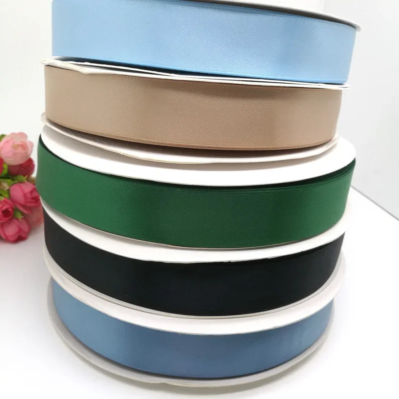 A stack of double face satin ribbon in various solid colors including blue, beige, cream, green, black, and gray.