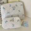 A white quilted cosmetic bag with blue bow print and the jolly house logo, shown in a studio setting.