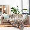 Graue Korallen-Fleecedecke mit orange-schwarzem Tiermuster über einem beigen Sofa.
