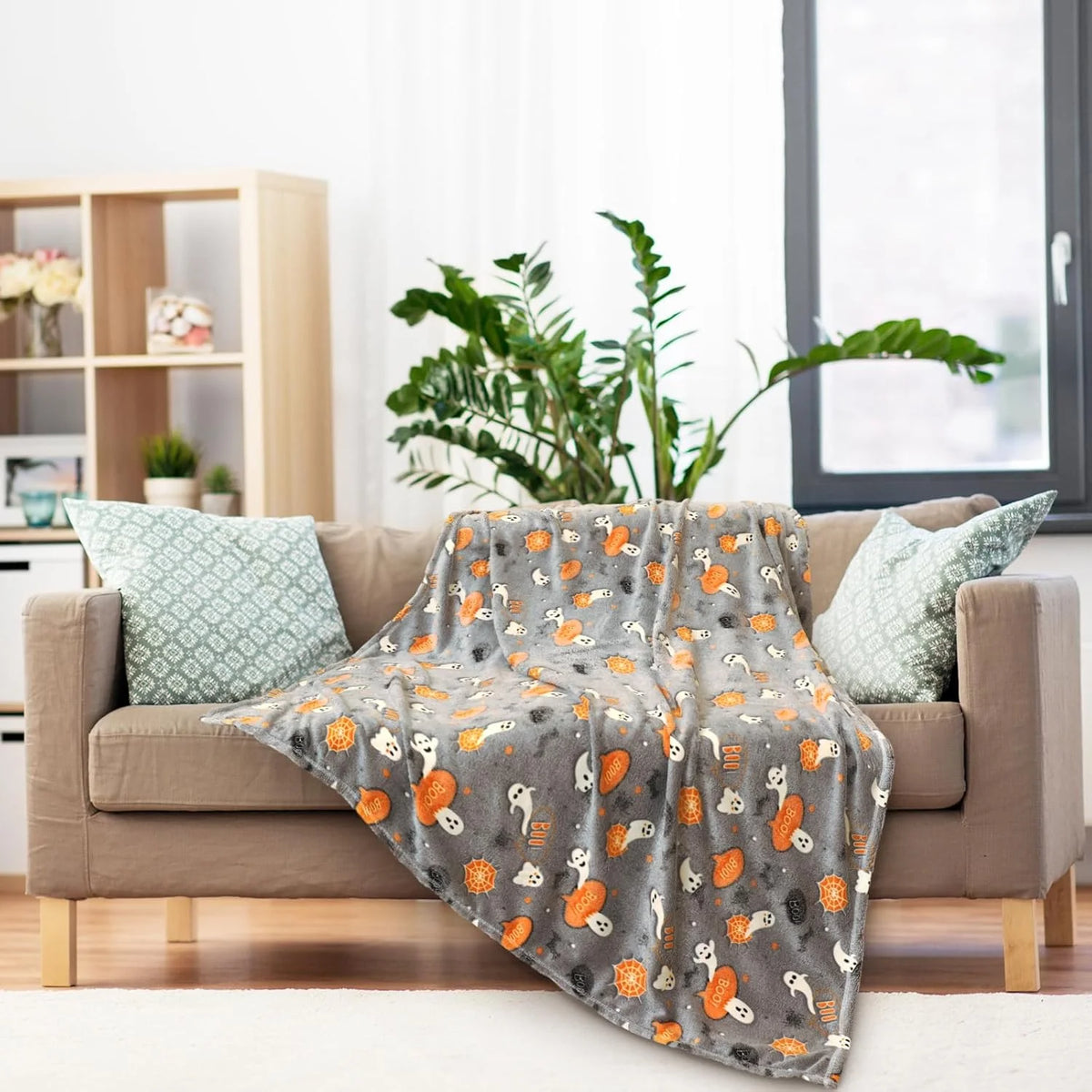 Graue Korallen-Fleecedecke mit orange-schwarzem Tiermuster über einem beigen Sofa.