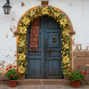 A rustic blue wooden door framed by a golden wreath of greenery and red berries on a white stucco wall.