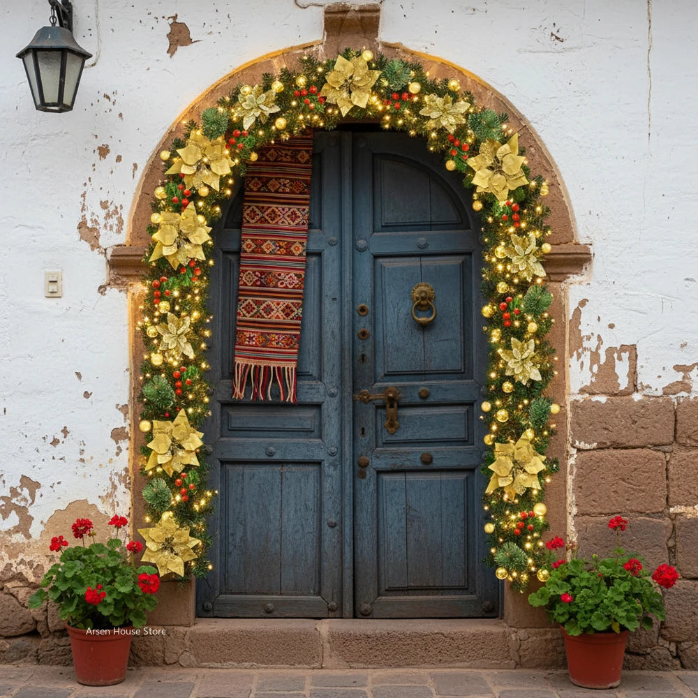 A rustic blue wooden door framed by a golden wreath of greenery and red berries on a white stucco wall.