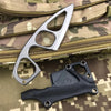 A silver fixed-blade neck knife is shown next to a black leather sheath on a camouflage fabric background.