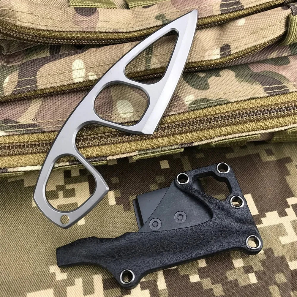 A silver fixed-blade neck knife is shown next to a black leather sheath on a camouflage fabric background.