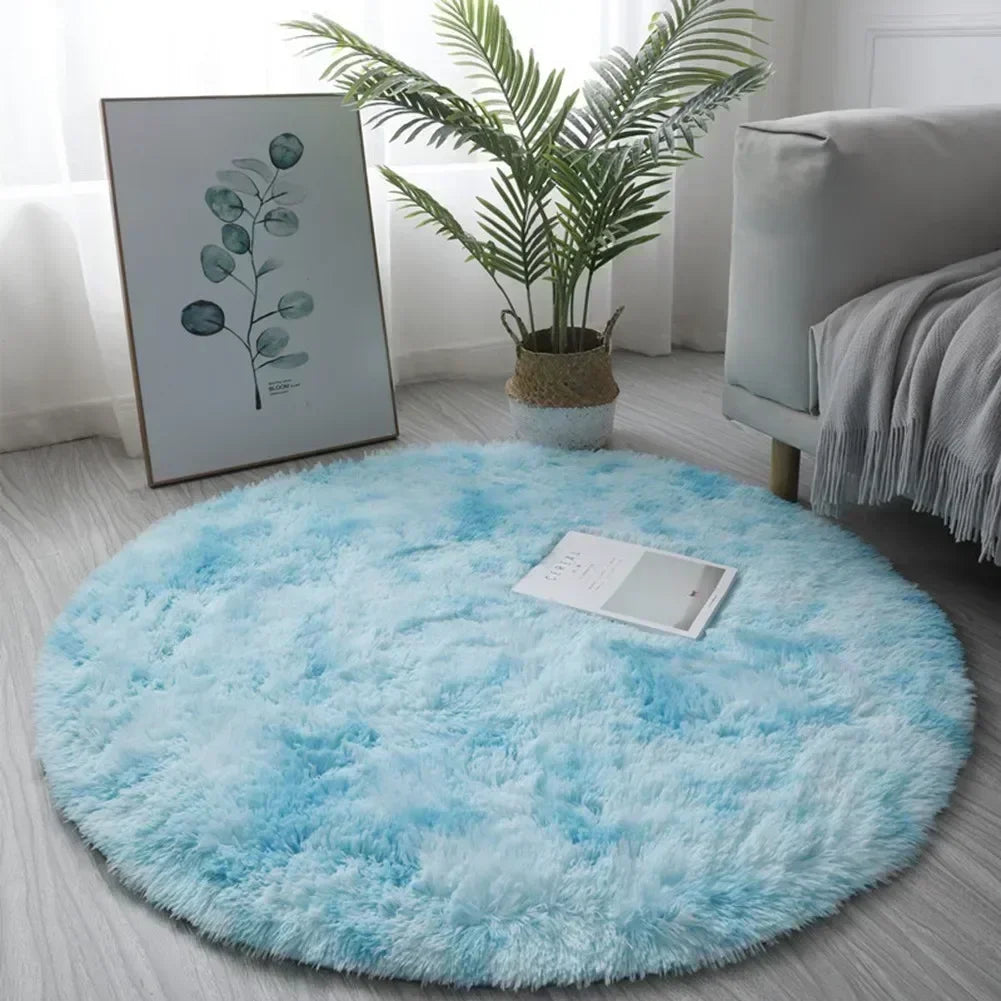 A bright blue shaggy circle area rug placed on a light gray floor with a potted plant and a sofa in the background.