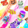 A hand is painting a purple water elf design onto a pink liquid surface with colorful paint and tools.