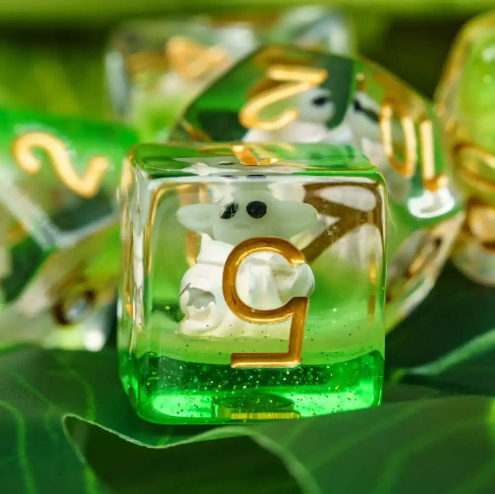 A close-up of a green resin dice set featuring white animal figures and gold numbers resting on a green leaf.