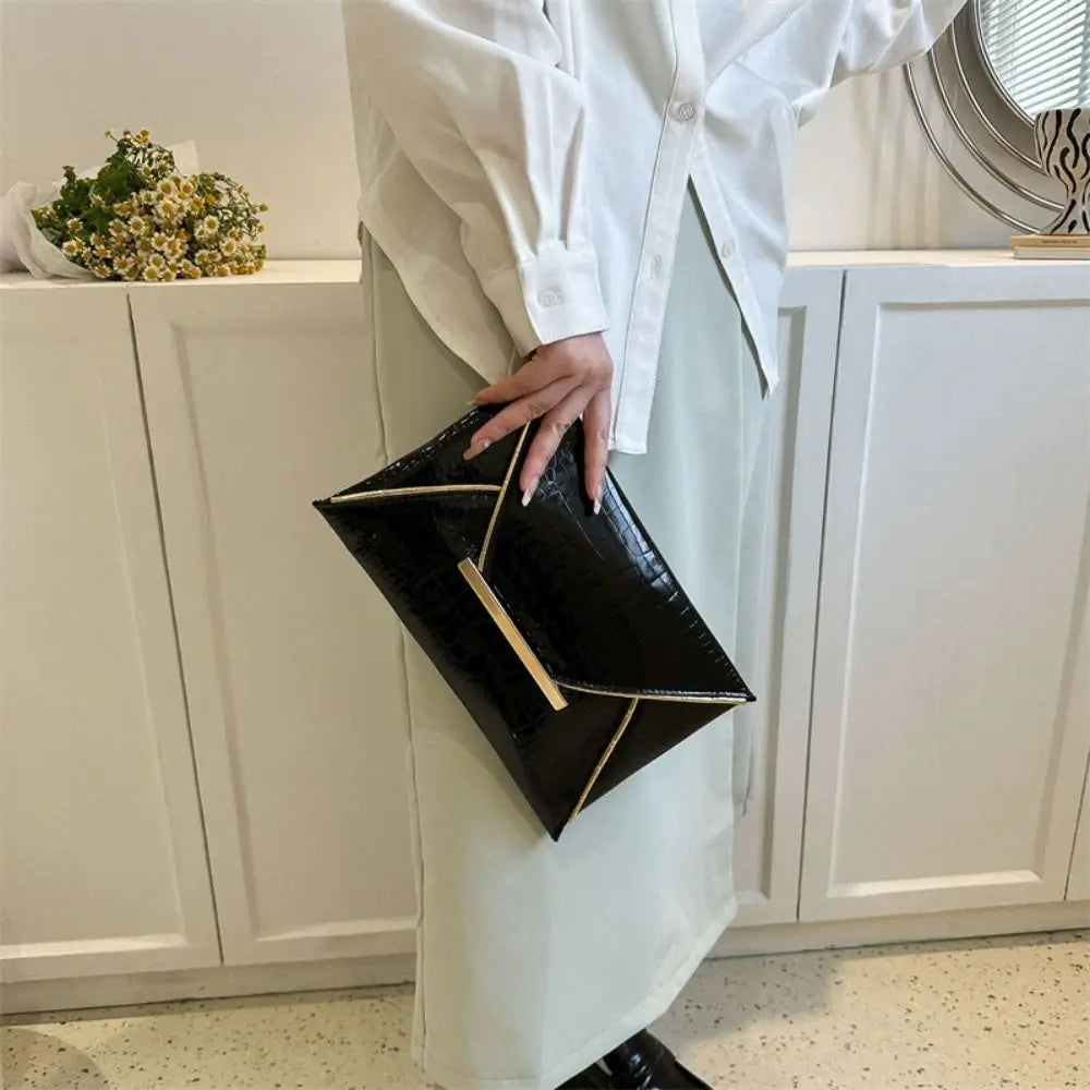 A person holds a black crocodile pattern PU envelope clutch with a coin pocket against a white cabinet backdrop.