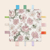 A white blanket featuring a floral pattern of pink and green roses and daisies, displayed on a wooden clothespin rack.