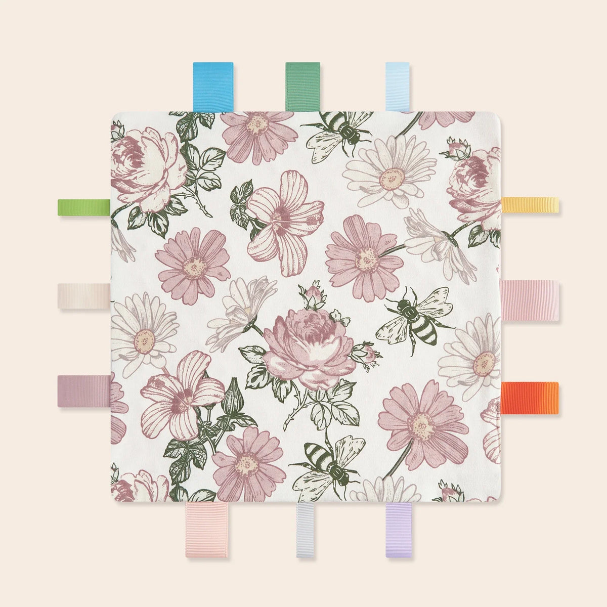 A white blanket featuring a floral pattern of pink and green roses and daisies, displayed on a wooden clothespin rack.