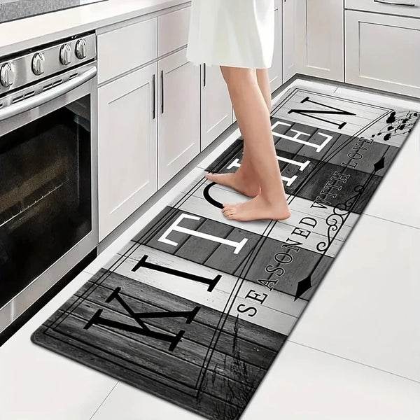 A woman stands on a black and white kitchen runner mat in front of white cabinetry and an oven.