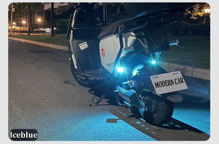 A white motorcycle is illuminated by a bright blue strobe light on the road at night.