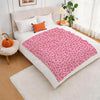 A pink leopard print flannel throw blanket is displayed on a bed with white linens and orange decorative pumpkins.