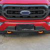 Close-up of a red Ford F-150 front bumper with black tow hook covers installed on the lower grille area.