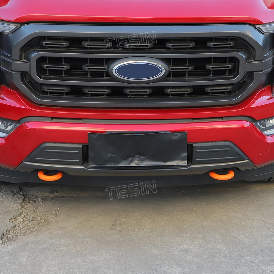 Close-up of a red Ford F-150 front bumper with black tow hook covers installed on the lower grille area.