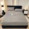 A gray plush mattress cover with an elastic edge is displayed on a black bed frame in a modern bedroom setting.