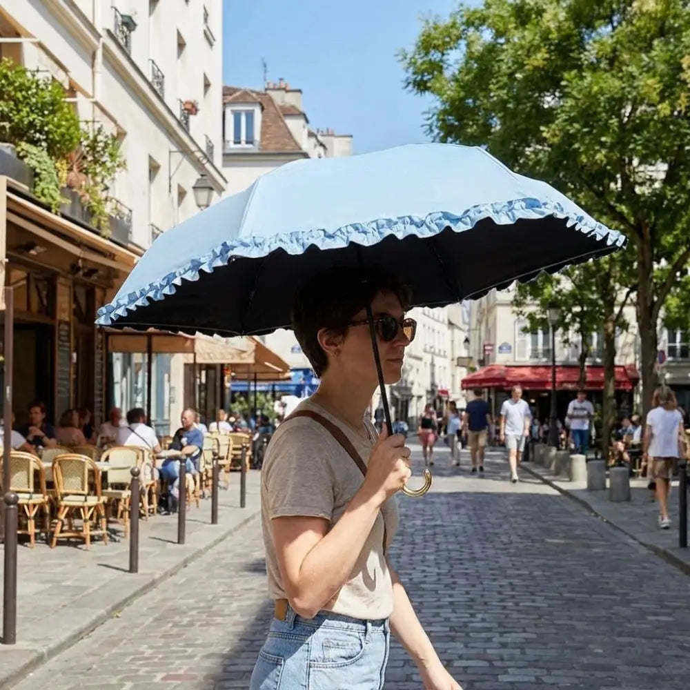 A person holding a blue and white lace umbrella on a sunny street with trees and buildings in the background.