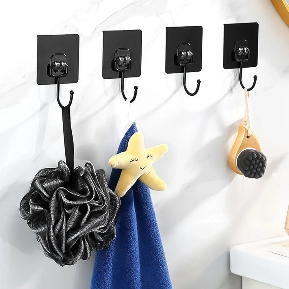 Black adhesive hooks hanging various items like a black sponge and a yellow starfish on a white marble surface