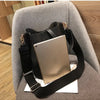 A tan leather crossbody bag with a black strap is resting on a gray upholstered chair.