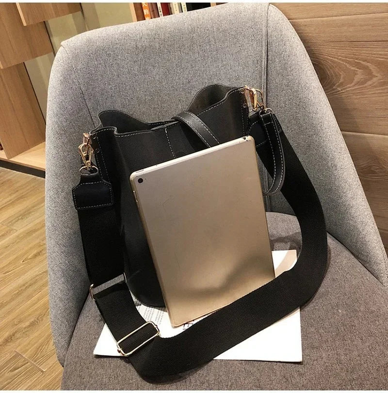 A tan leather crossbody bag with a black strap is resting on a gray upholstered chair.