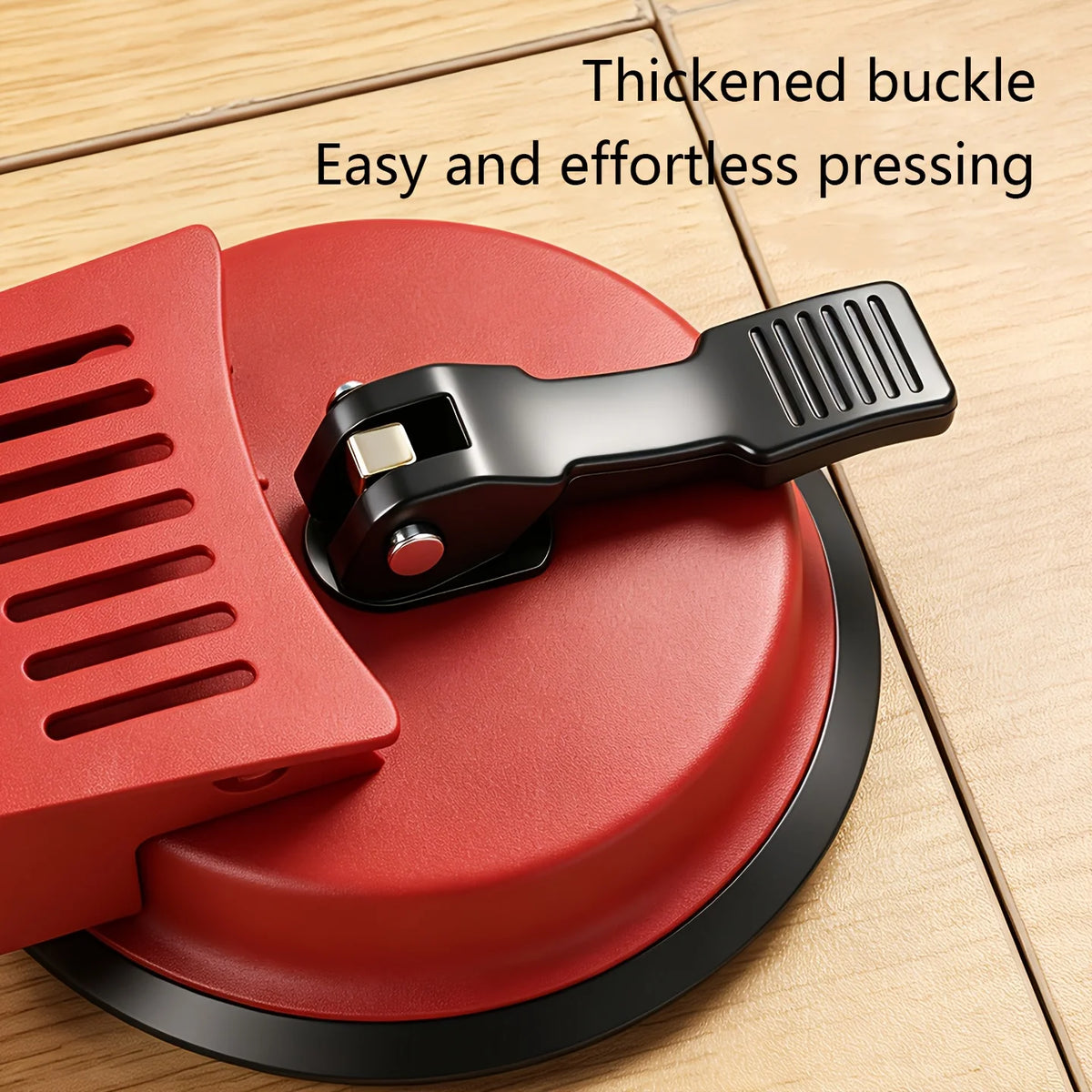 A red floor gap fixer tool with a black buckle is shown on a wooden surface.