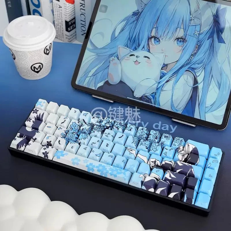Gros plan d'un clavier mécanique avec des touches Raven Sakura bleu et blanc, placé à côté d'un ordinateur portable et d'un