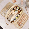 A beige cosmetic bag filled with various makeup products including lipsticks and a powder compact on a light surface.