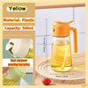 An orange plastic oil spray bottle with a yellow liquid, shown next to a red tomato on a wooden surface.