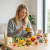A woman is assembling a set of cute micro building blocks figurines shaped like desserts and food items on a wooden table.