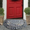 A vintage stone tile doormat with an intricate pattern lies on a gray stone step in front of a red door.