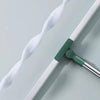 A silicone scraper broom and squeegee tool with a white flexible strip and a green handle on a light gray surface.