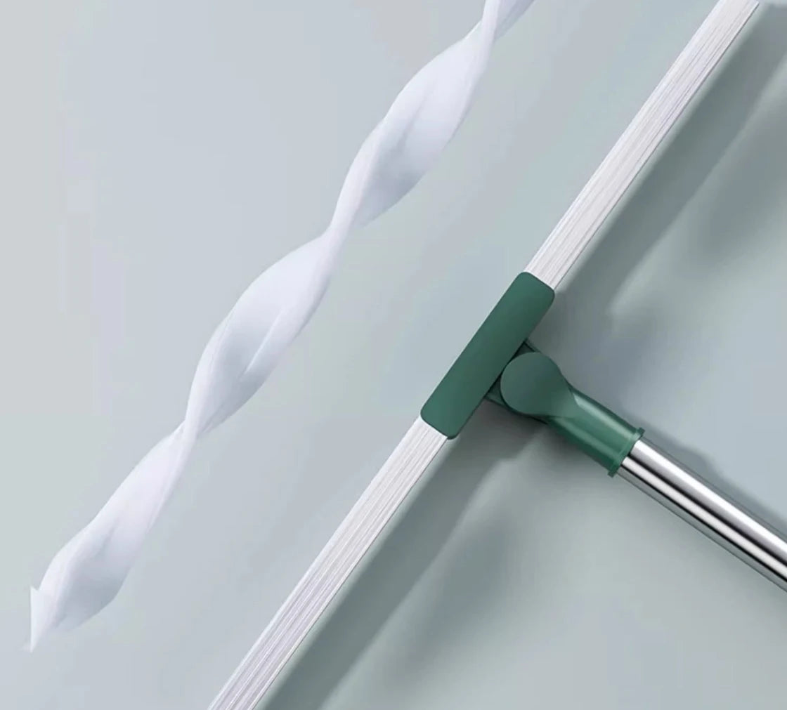 A silicone scraper broom and squeegee tool with a white flexible strip and a green handle on a light gray surface.