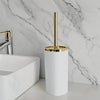 A tall white toilet brush set with a gold rotating stand is displayed on a marble countertop.