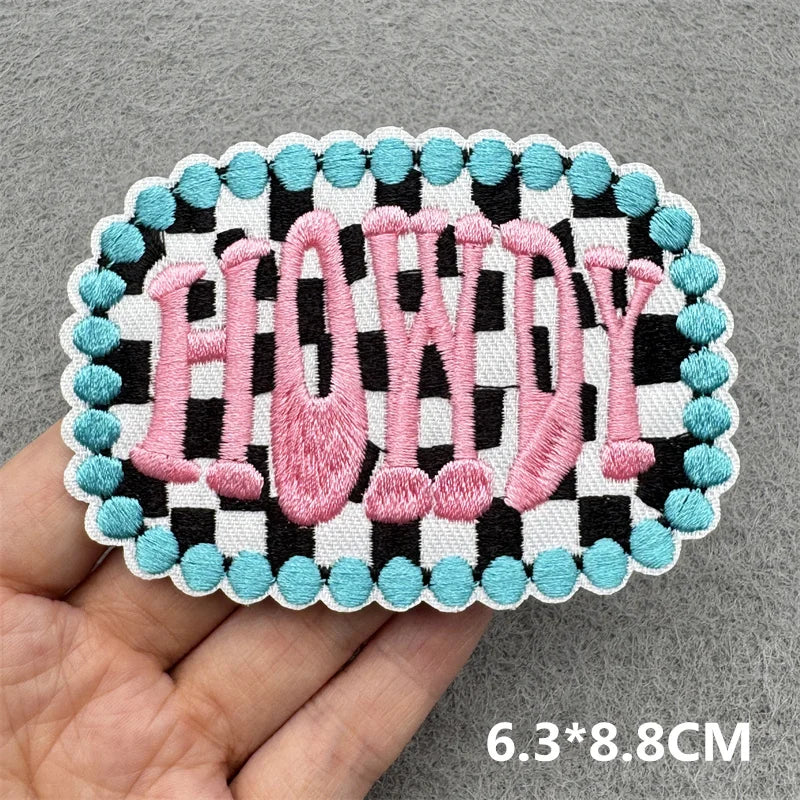 Pink embroidered patch spelling HOWDY with a black and white checkered border on a gray background.