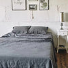 A gray linen bed sheet set is spread on a bed, with pillows and a draped cover visible.