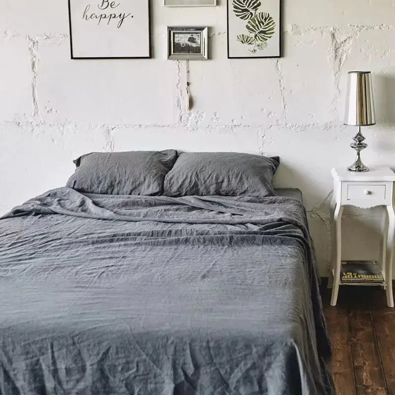 A gray linen bed sheet set is spread on a bed, with pillows and a draped cover visible.