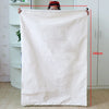 A large, off-white heavy-duty canvas laundry bag hanging vertically against a white cabinet.