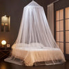 A sheer white ceiling-hung dome mosquito net covering a bed in a dark room.