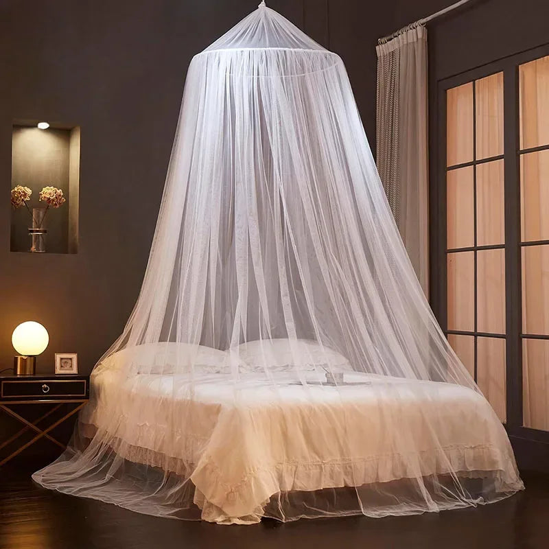 A sheer white ceiling-hung dome mosquito net covering a bed in a dark room.