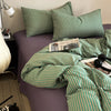 A green and gold striped duvet cover set with matching pillowcases on a purple bed.