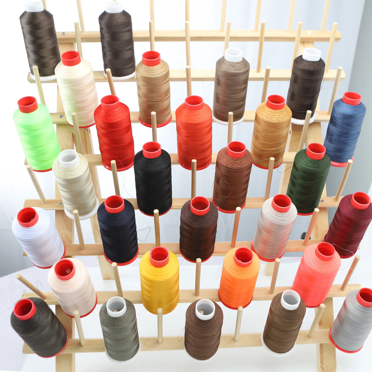 A collection of various colored heavy-duty nylon bonded thread spools arranged on wooden sticks.
