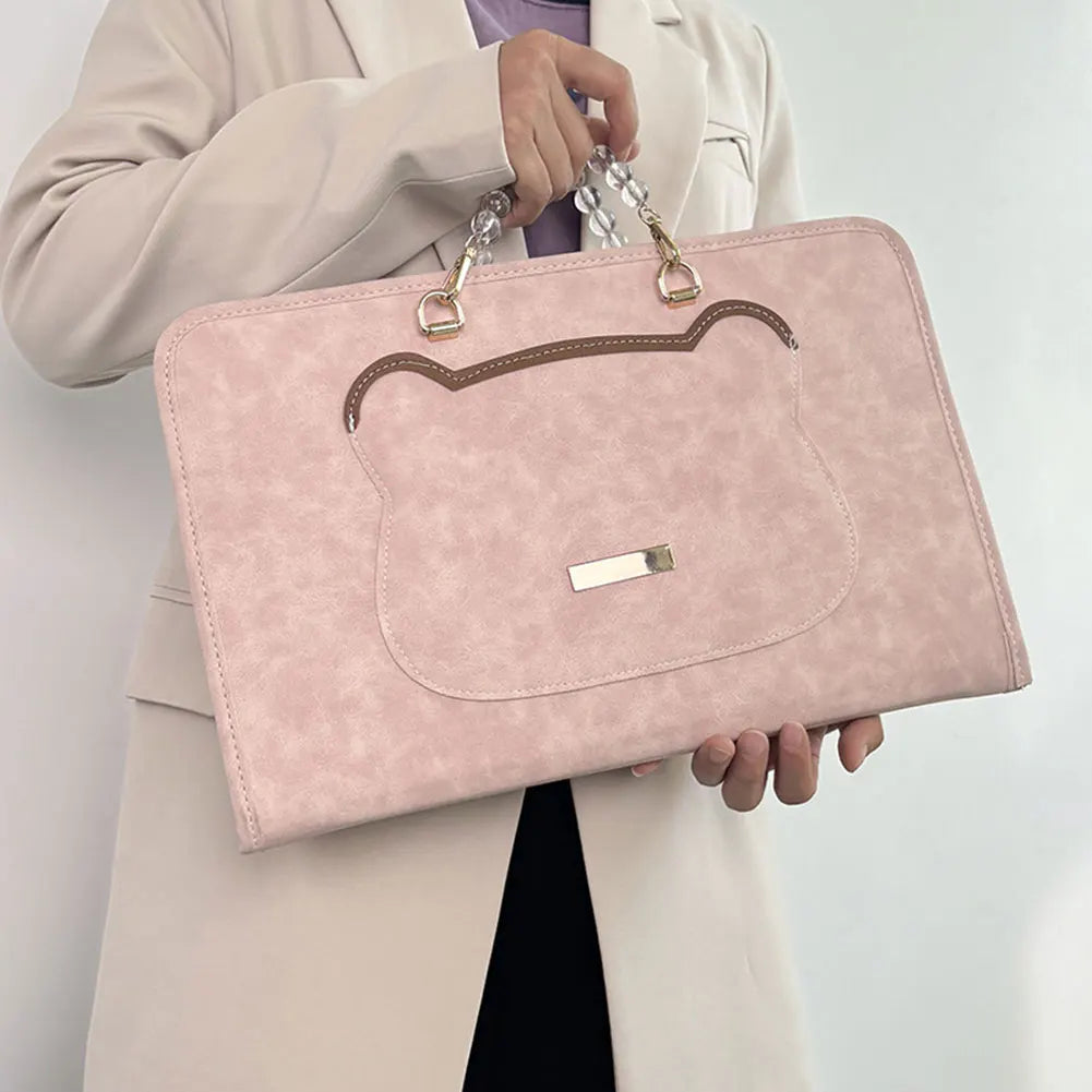 A light pink water-resistant laptop briefcase with gold hardware is held by a person wearing a beige blazer.