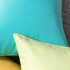 A close-up of three cushion covers in shades of turquoise, lime green, and yellow.
