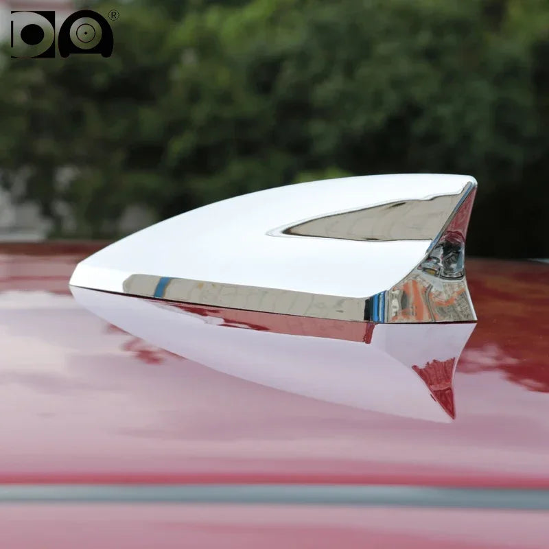 A silver shark fin car antenna with a heart shape is mounted on a red car body.