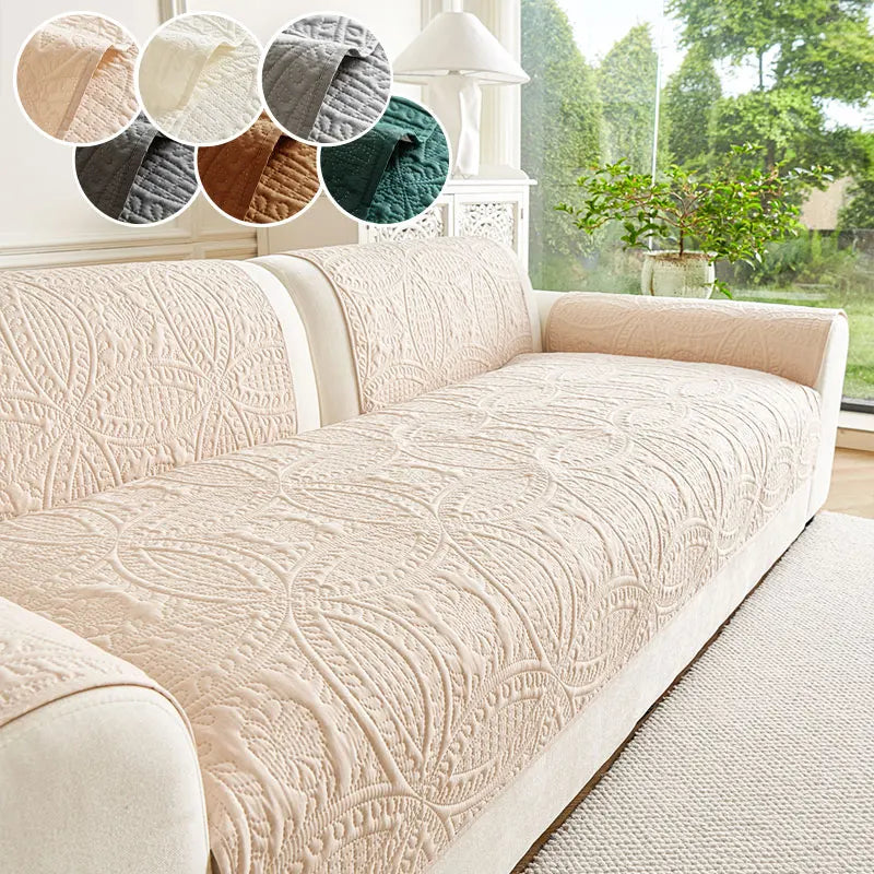 A cream anti-slip sofa cover is displayed with various fabric swatches and a potted plant in a bright room.