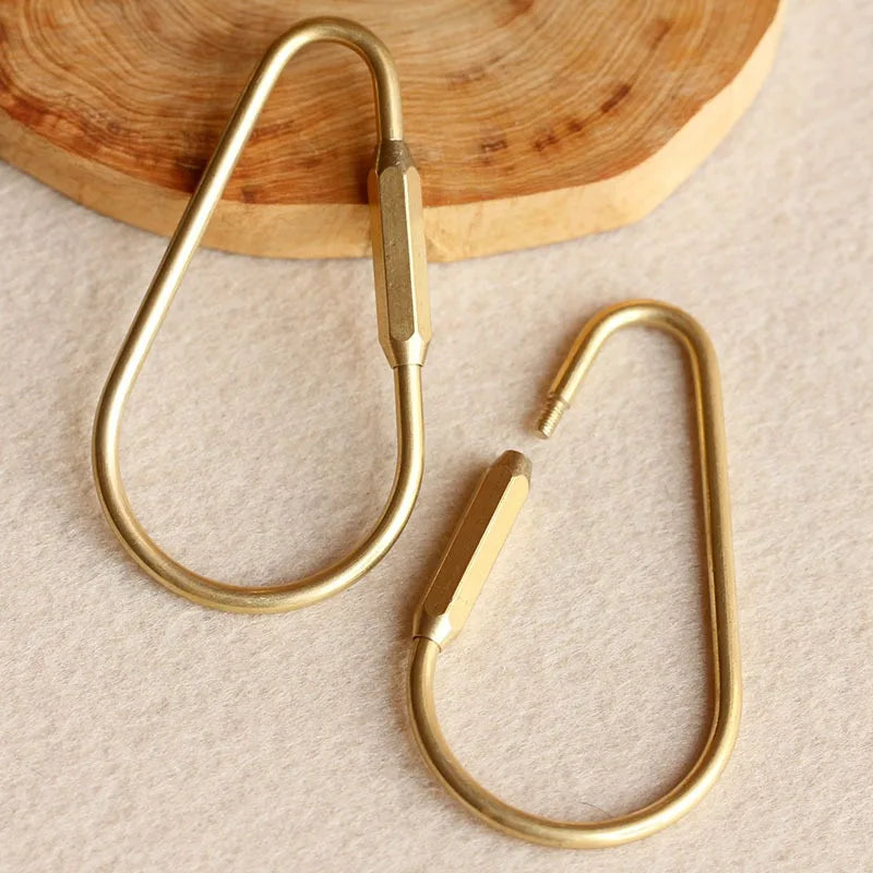 A set of gold brass keychain charms with locking carabiner clips resting on a light surface.