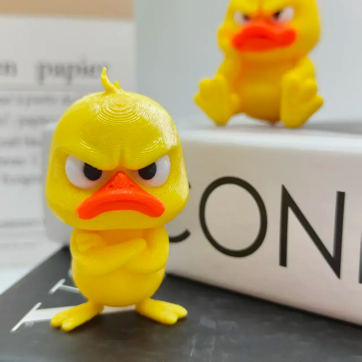 A yellow 3D printed duck statue decoration with an angry expression sitting on a dark surface.