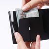 Hands holding a black slim leather card holder with US dollar bills inside.